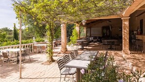 An outdoor patio area with tables and chairs, surrounded by trees and a pergola. - Camping Domaine De Chanteraine (Aiguines)