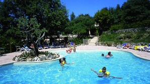 A swimming pool with clear blue water, surrounded by lounge chairs and a stone wall. - Camping Domaine De Chanteraine (Aiguines)