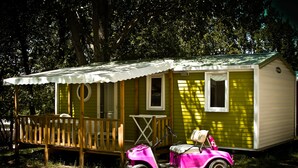 A small, single-story mobile home with a porch and a pink toy car parked in front. - Camping Domaine De Chanteraine (Aiguines)