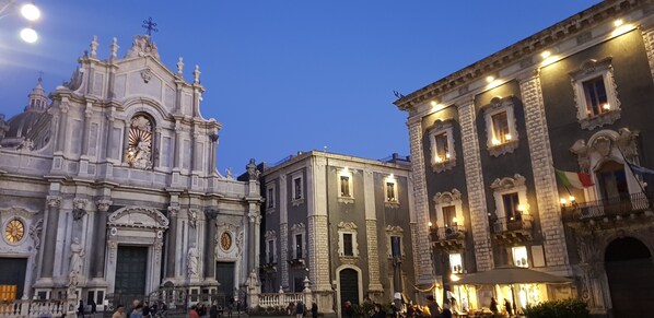 A historic building with ornate architecture, a prominent clock, and a well-lit entrance. - Tre Stelle al Duomo (Catania)