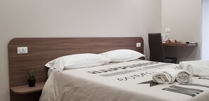 A neatly made bed with white bedding and a pillow, a small potted plant on a nightstand, and a towel on the bed. - Tre Stelle al Duomo (Catania)