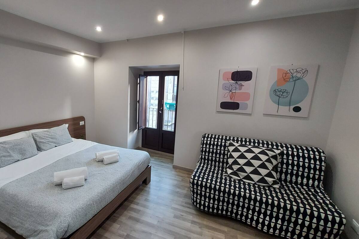 A modern bedroom with a bed, a black and white patterned sofa, and two abstract wall art pieces.