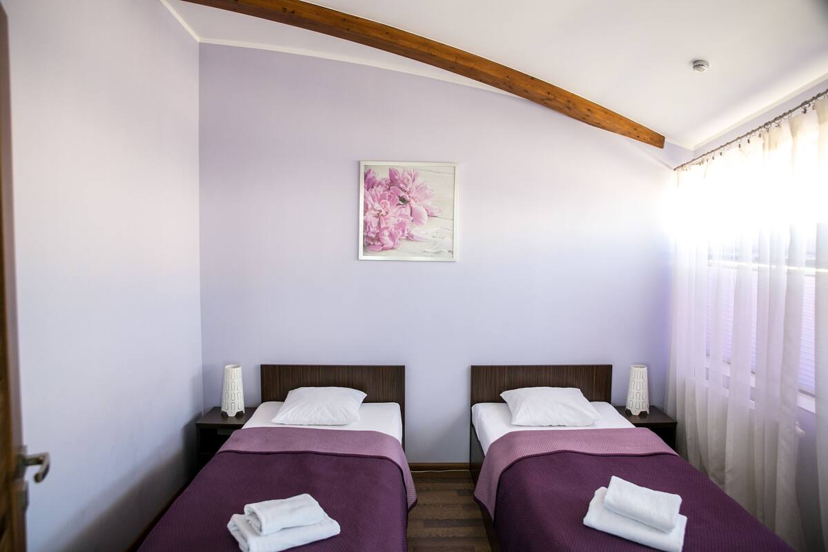 Ein Zimmer mit zwei Betten, einem Holzbalken an der Decke, einem Wandbild und einem Fenster mit Vorhängen.