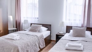 Habitació d'hotel amb dos llits, una meseta de nit amb una làmpada, una cadira i una finestra amb cortines.