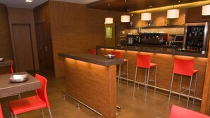 Una cocina moderna con una isla central, taburetes rojos y una zona de bar con cafetera.