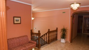 Un vestíbulo con un sofá rojo, una mesa de centro de madera, una escalera con barandilla de madera y una planta en maceta.