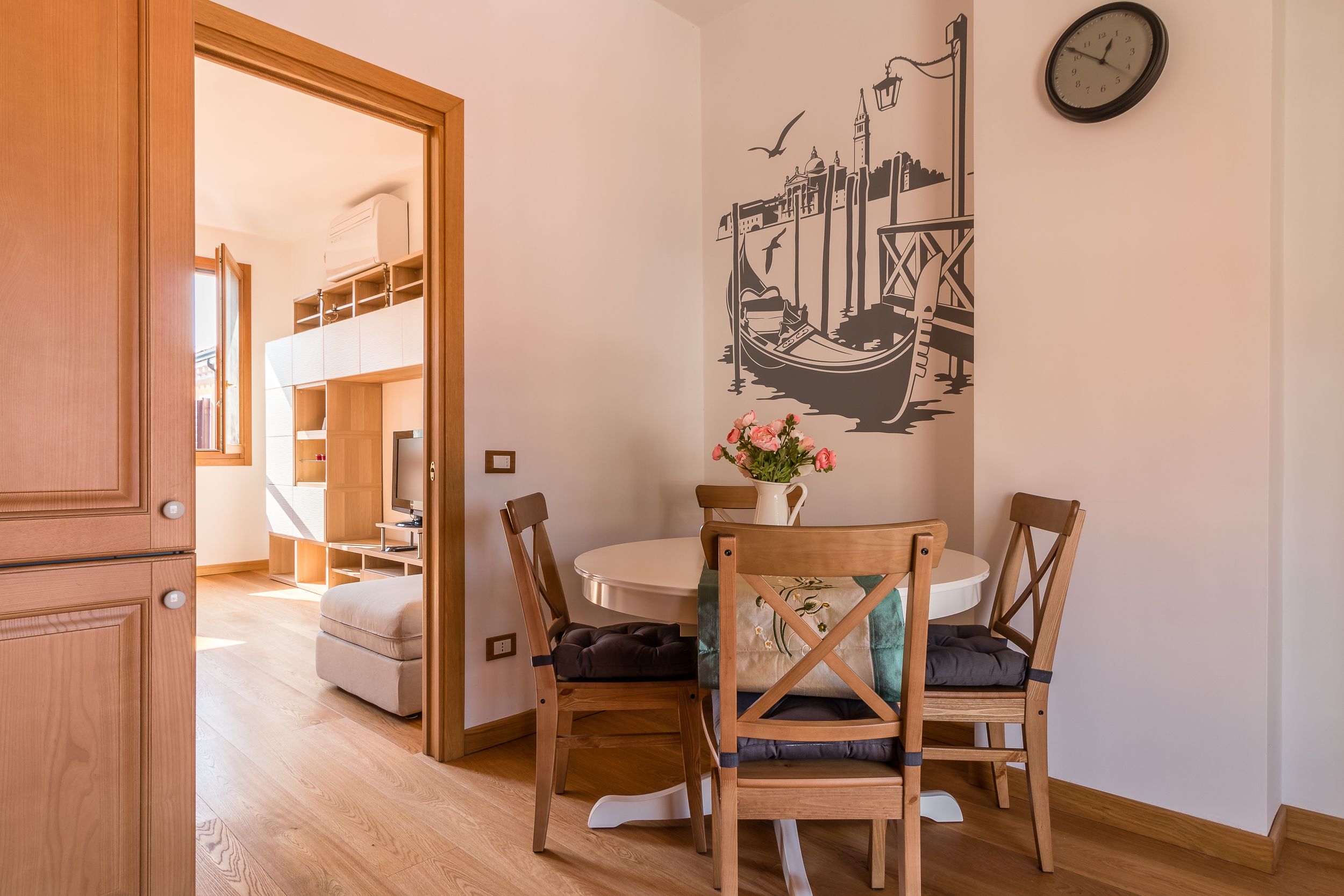 A dining area with a round table, two wooden chairs, and a wall-mounted clock.