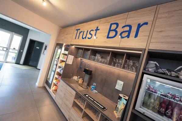 Un bar Trust con mostrador de madera, estantes con cristalería y un refrigerador con bebidas.