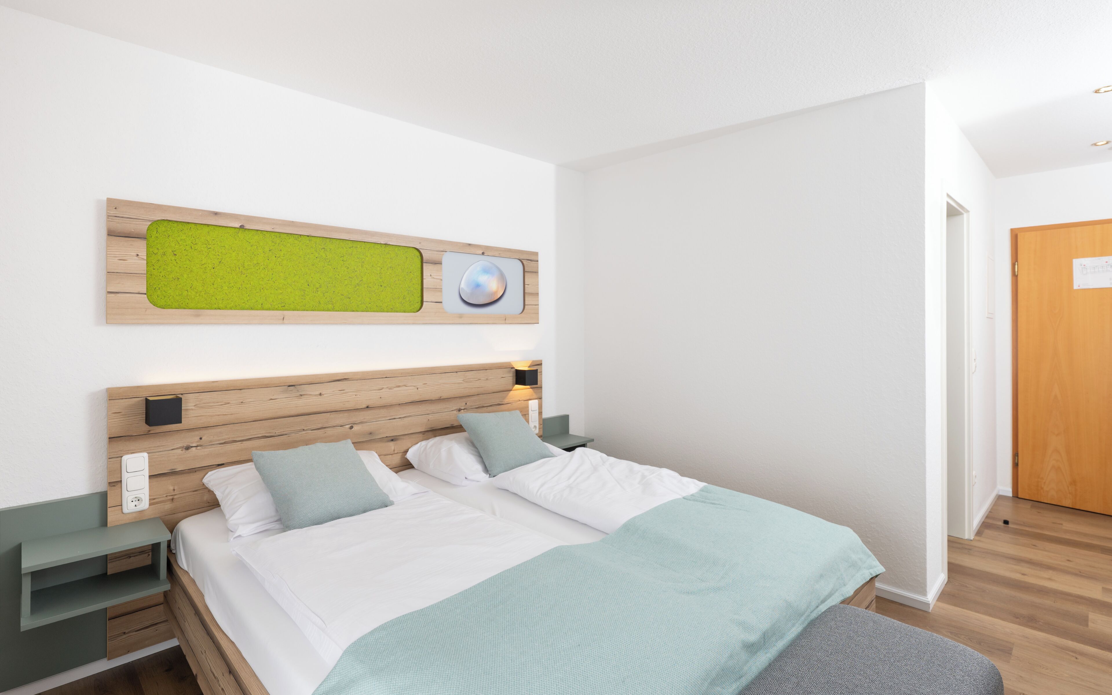 Une chambre moderne avec une tête de lit en bois, un mur d’accent vert, un lit avec du linge de lit blanc et un banc gris.