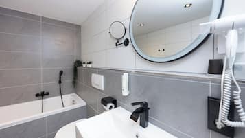 A modern bathroom with a bathtub, a sink, a mirror, and a hairdryer.