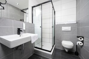 Un baño moderno con ducha de vidrio, lavamanos blanco y retrete.