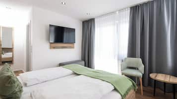 Ein Hotelzimmer mit Bett, Wandfernseher, Stuhl, einem kleinen Tisch und einem Fenster mit Vorhängen.