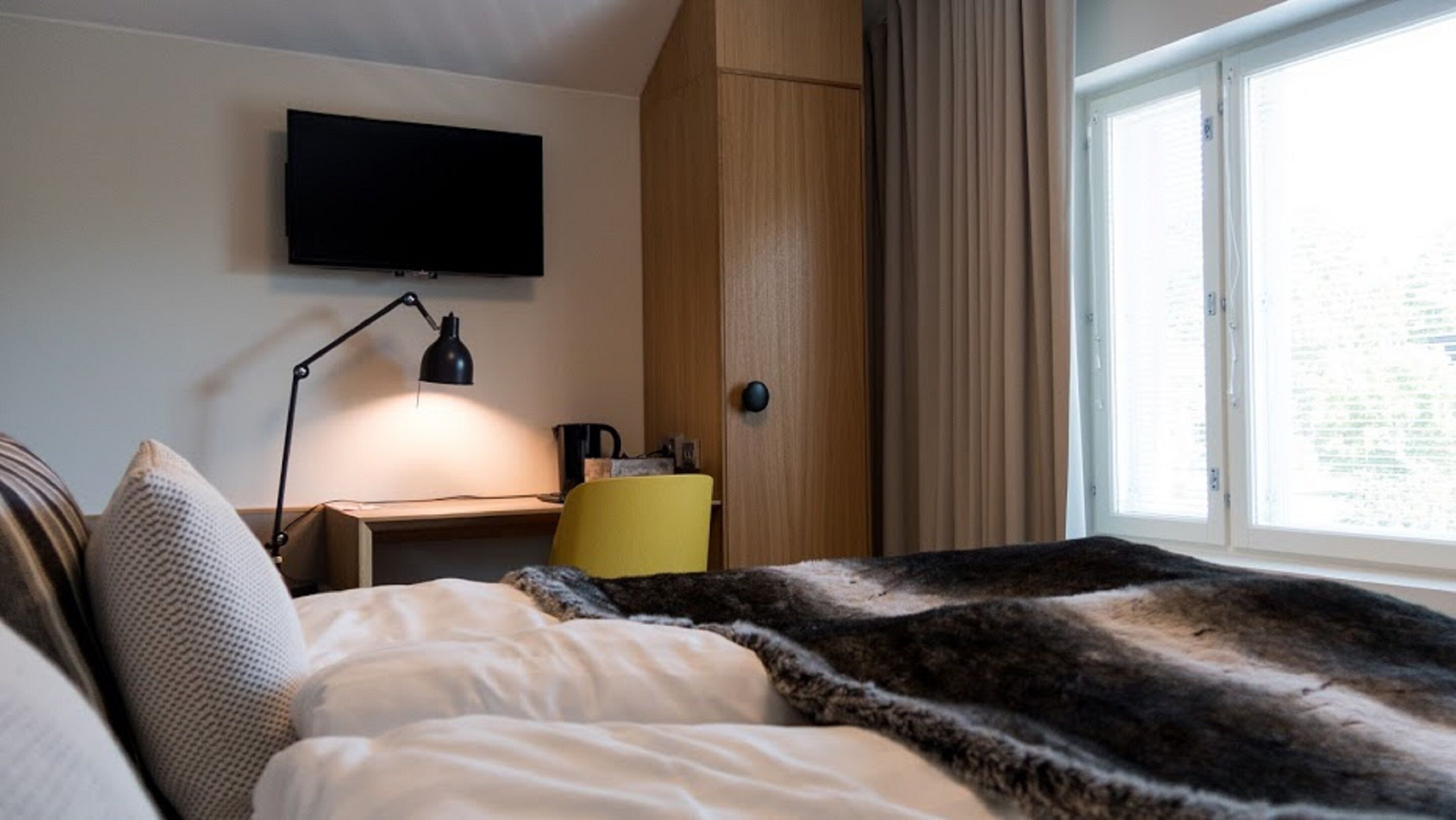 A bedroom with a bed, a desk, a chair, a television, and a window with curtains.