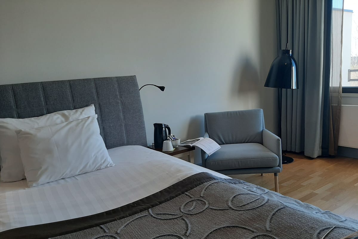 Una habitación de hotel con una cama, una silla, una cafetera y una lámpara.