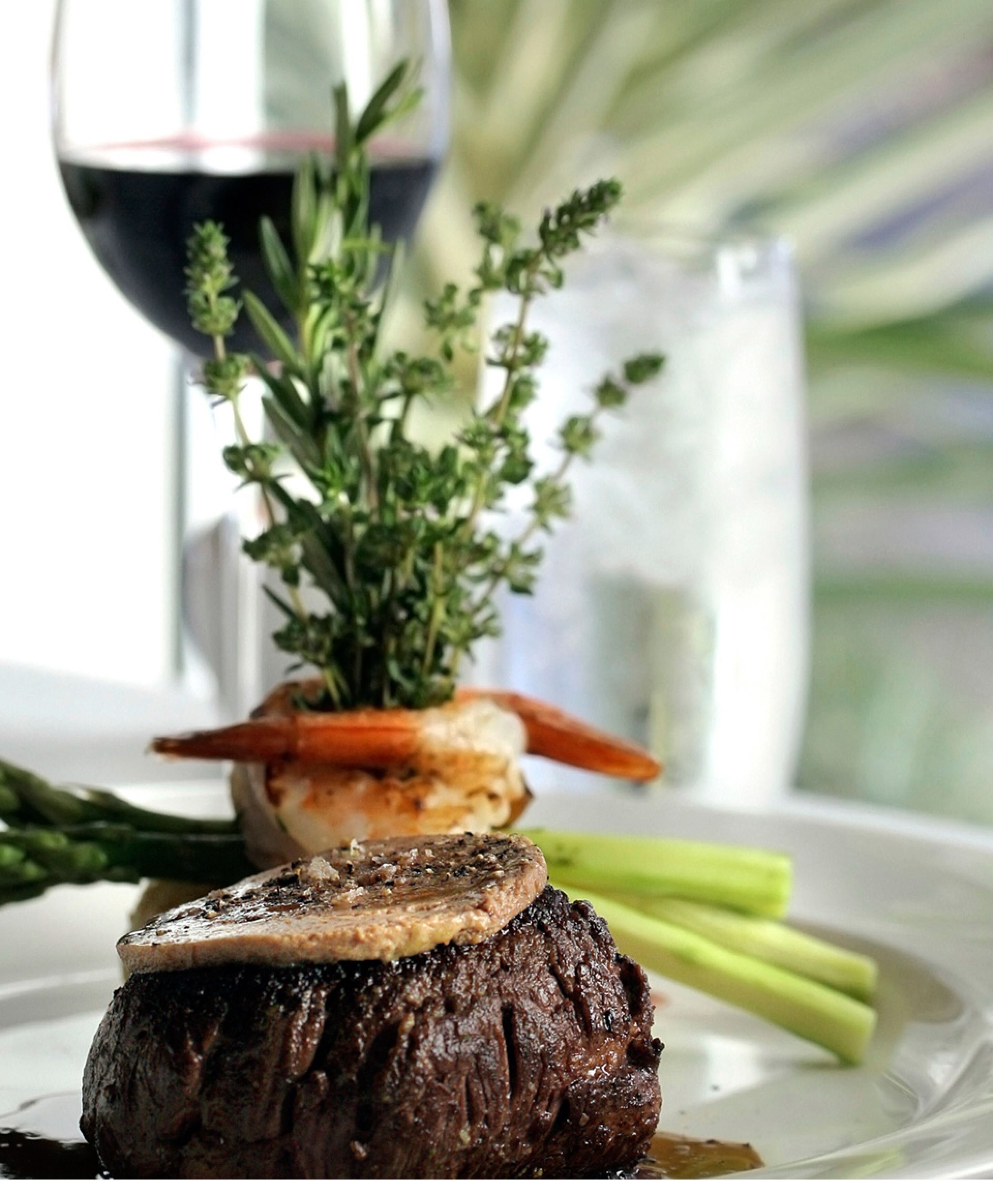 Un plato con bistec, champiñón, hierbas, espárragos y una copa de vino tinto.