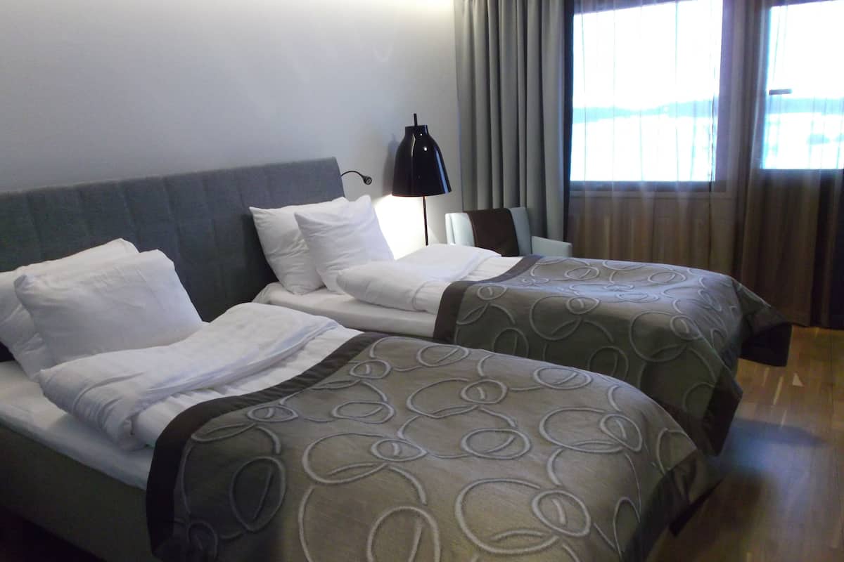 Una habitación de hotel con dos camas, un escritorio, una lámpara y una ventana con cortinas.
