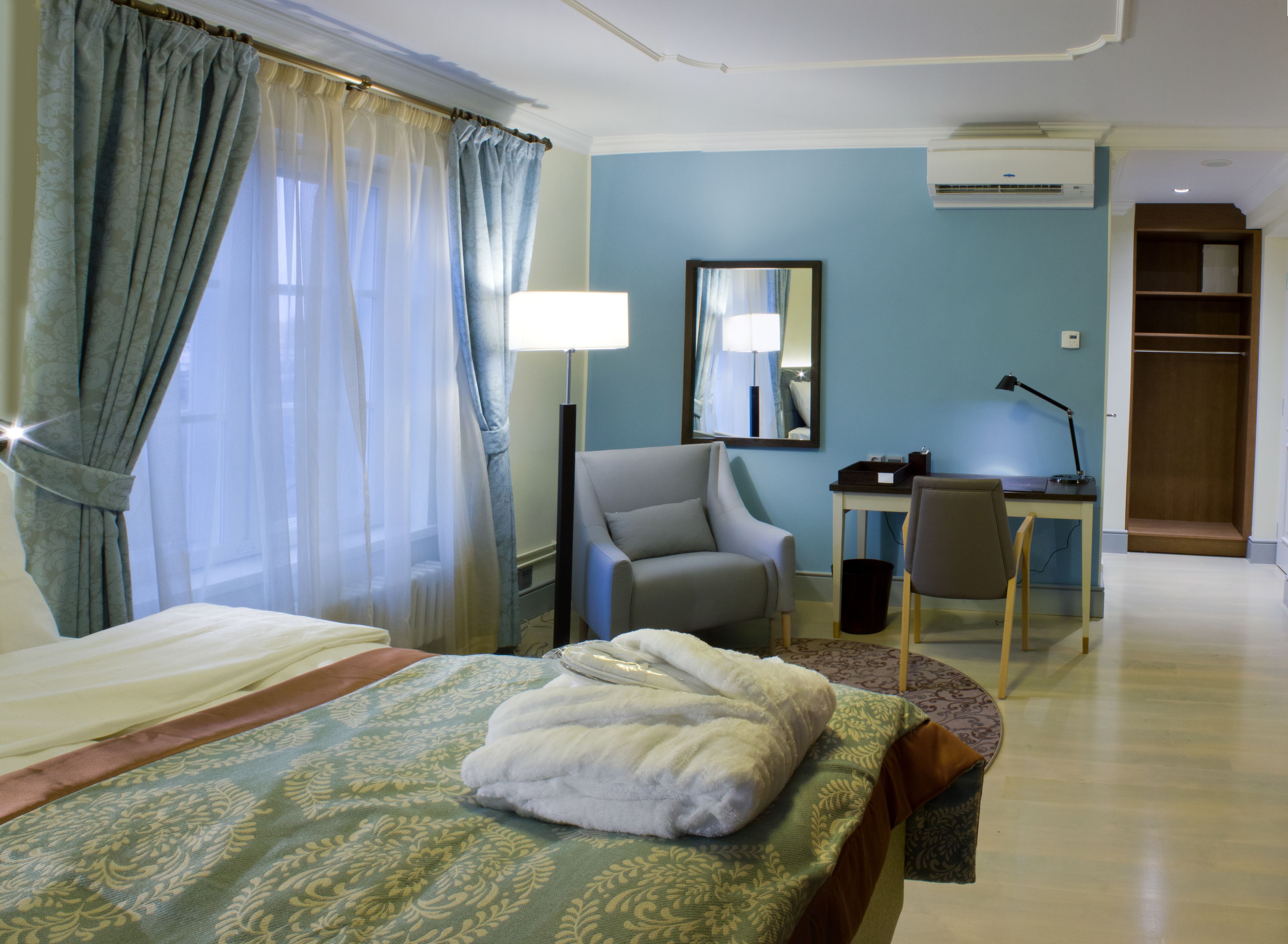 A hotel room with a bed, a desk, a chair, a mirror, and a wardrobe.