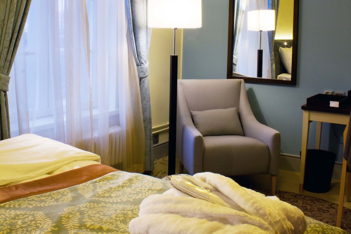 Una habitación de hotel con cama, una silla, una lámpara y un espejo.