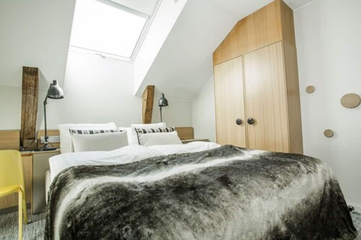 Un dormitorio con tragaluz, una cama con colcha blanco y negro, un armario de madera y una silla amarilla.