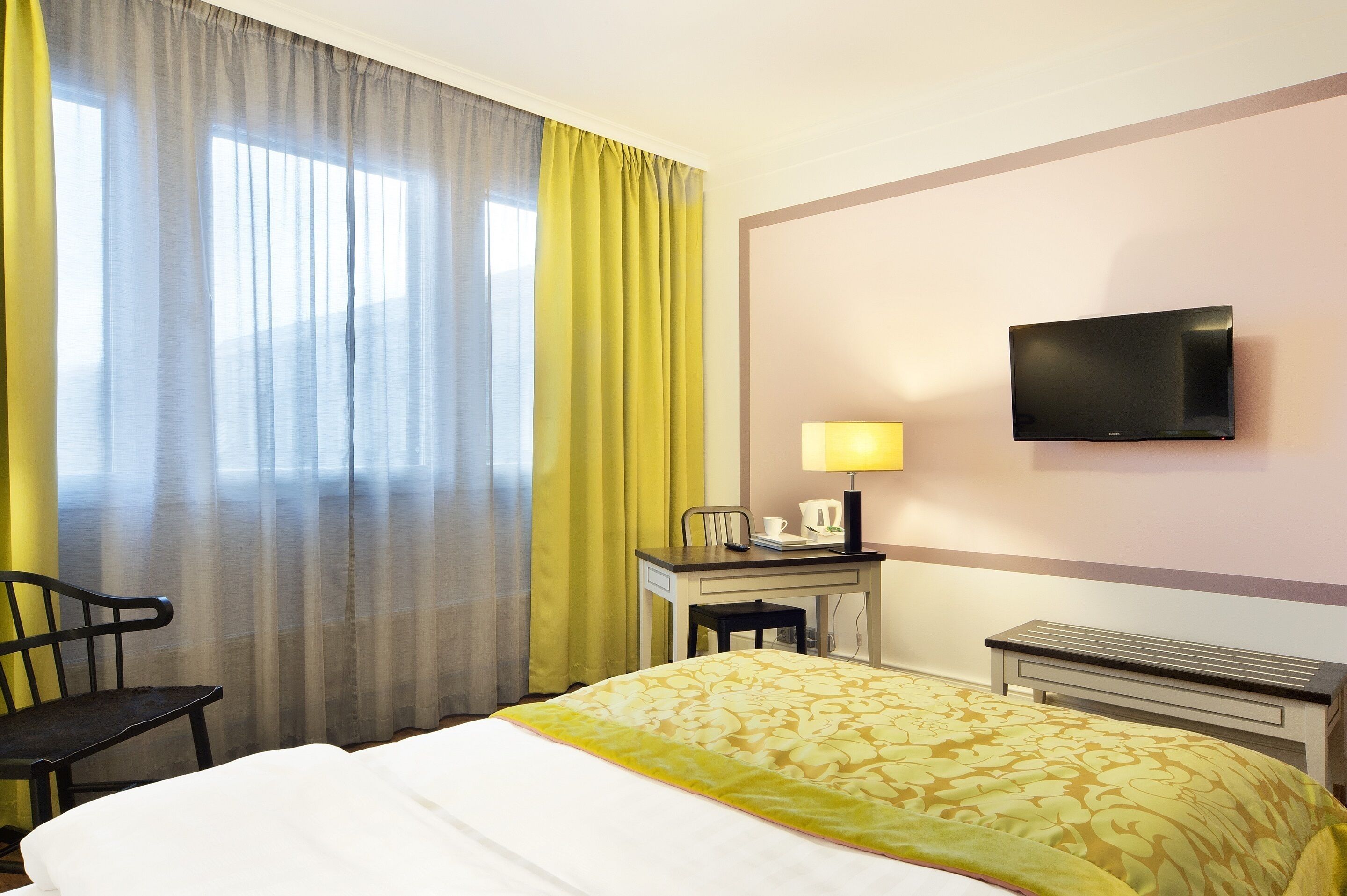 A hotel room with a bed, a desk, a chair, a television, and a window with curtains.