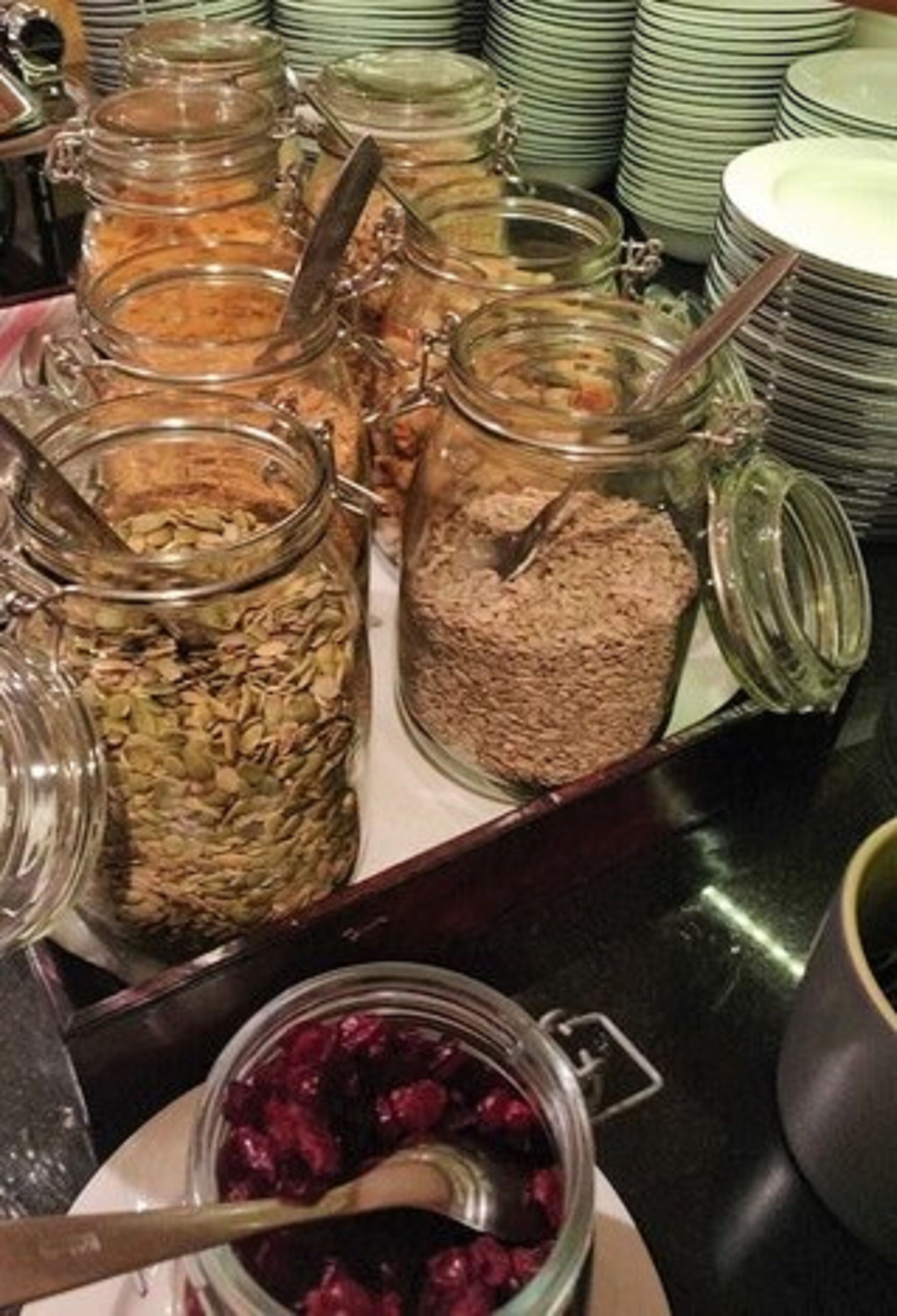 Un bufé con diversos alimentos en recipientes de vidrio y un bol de compota de frutas rojas.