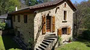 Una casa in pietra con persiane di legno, un camino e una piccola scala che conduce all'ingresso.