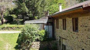 Un edificio in pietra con tetto in tegole, circondato da un prato curato e alberi alti.
