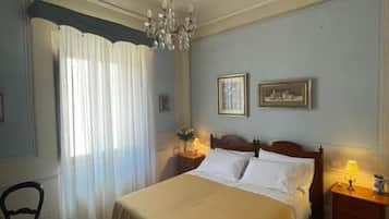 A bedroom with a bed, a chandelier, a nightstand, and a chair.