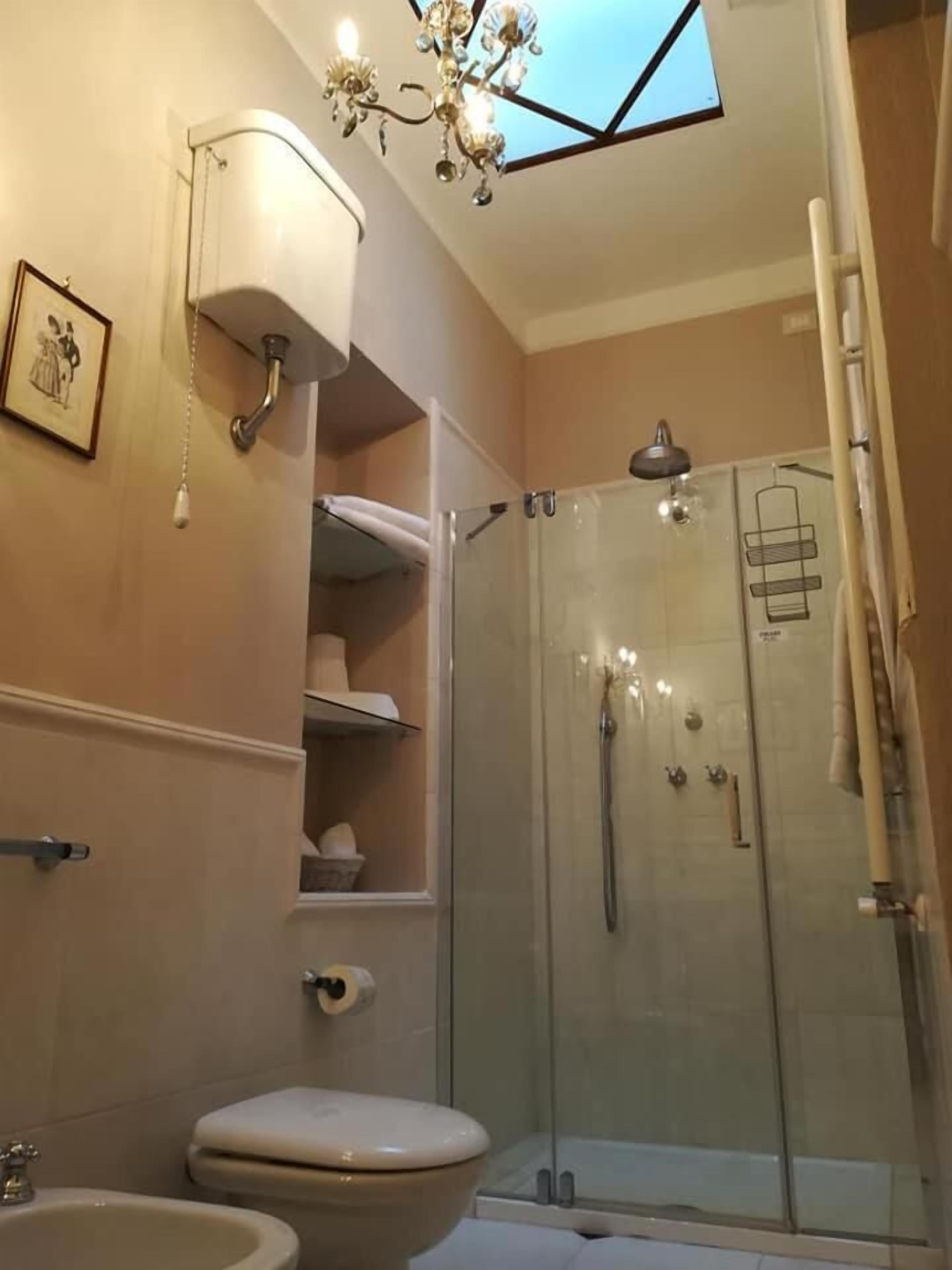 A modern bathroom with a glass-enclosed shower, a toilet, a sink, and a chandelier.