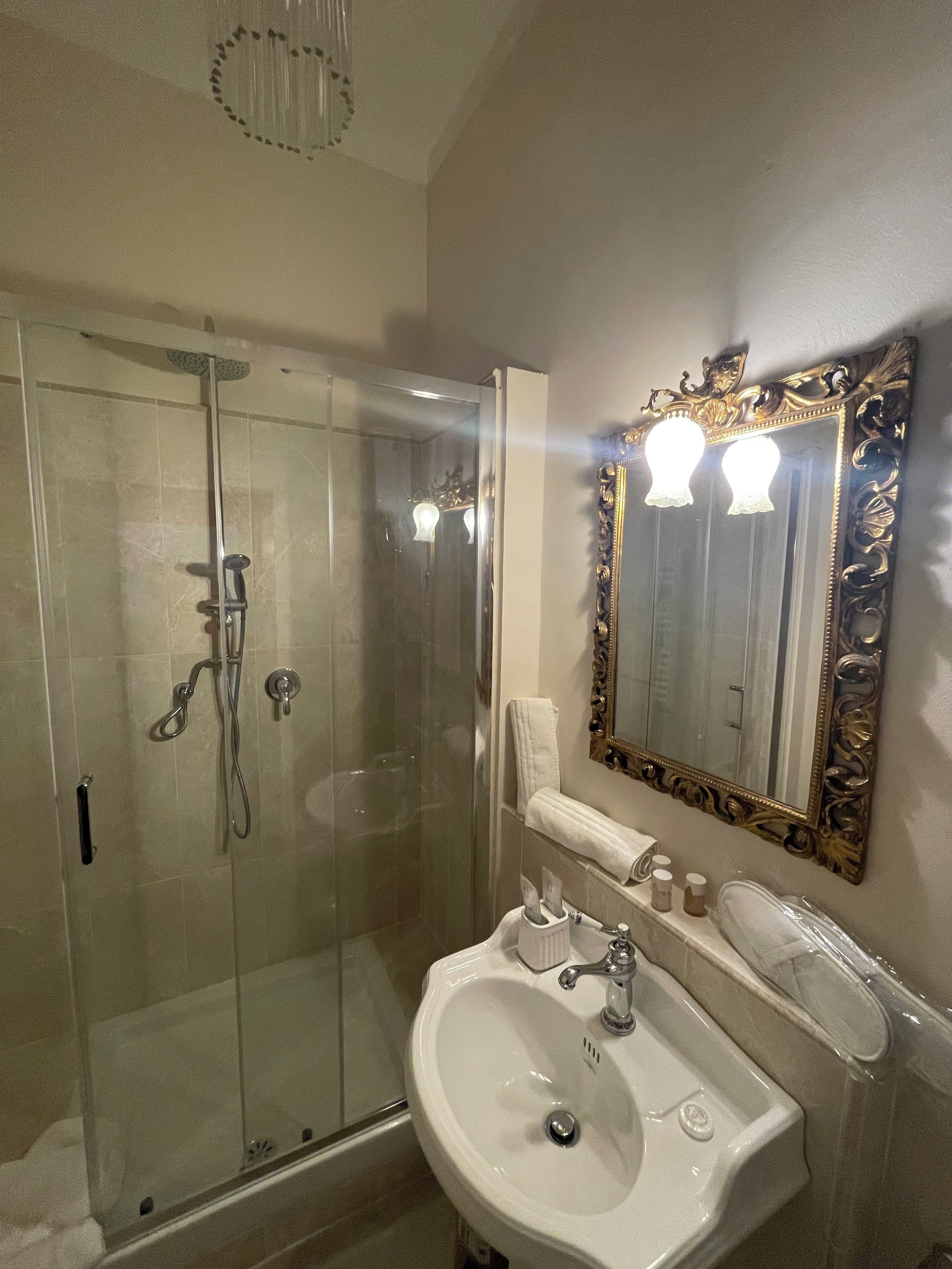 A bathroom with a glass-enclosed shower, a white sink, and a large ornate mirror.