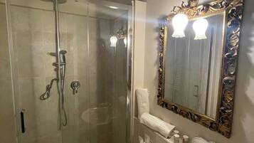 A bathroom with a glass-enclosed shower, a white sink, and a large ornate mirror.