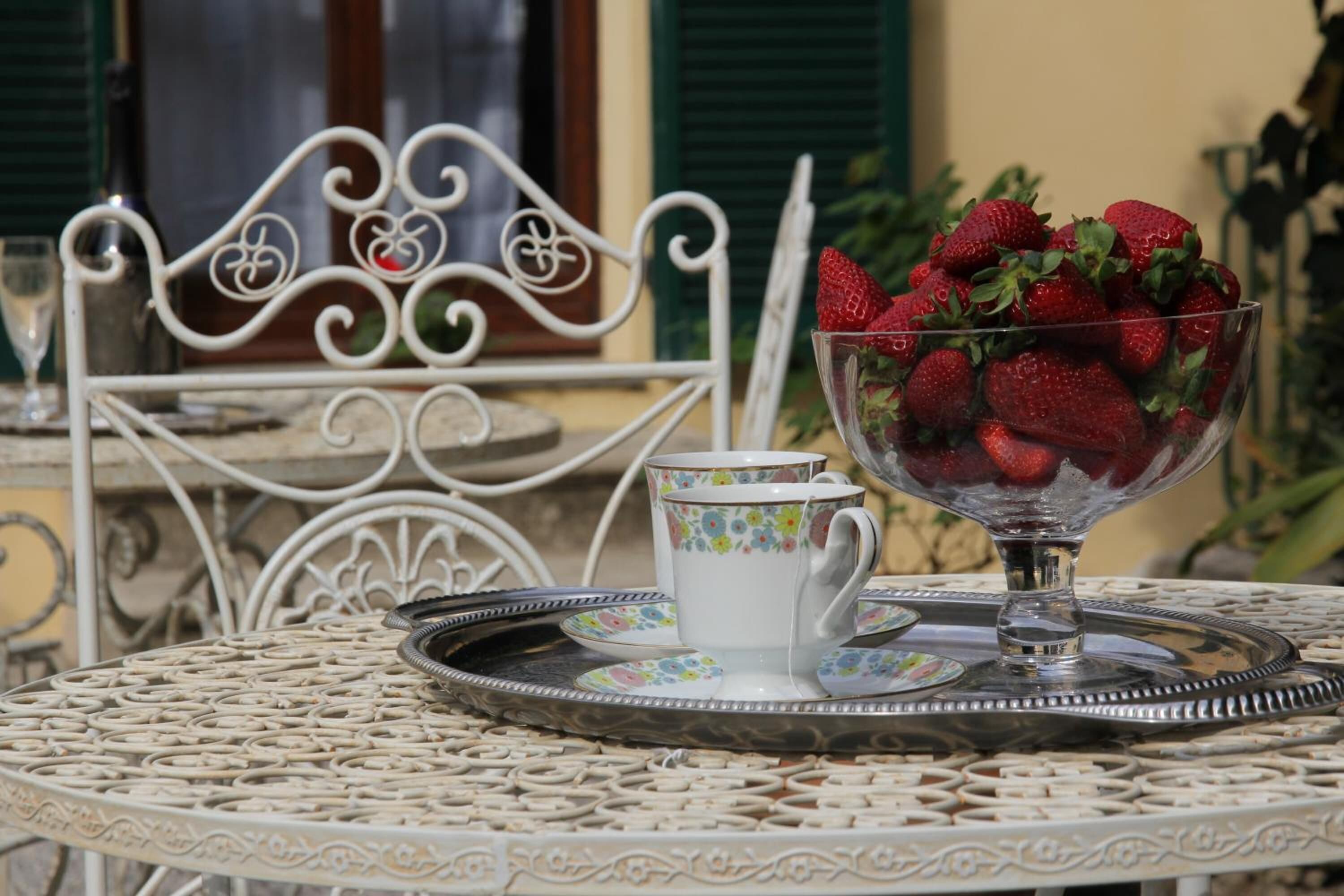 A table with a decorative metal tray, a glass bowl of strawberries, and a floral-patterned cup and saucer.