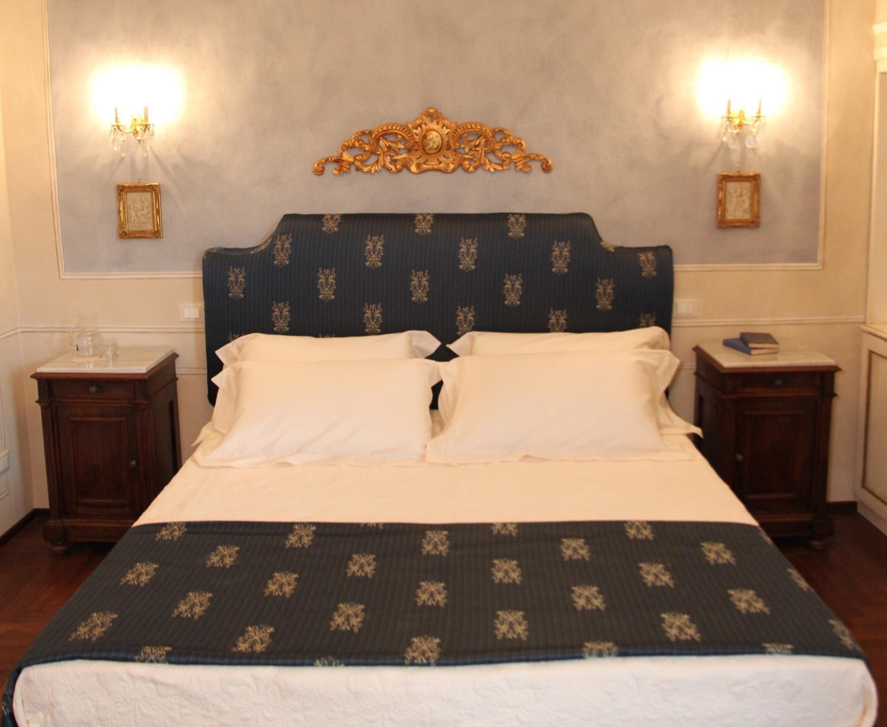 A neatly made bed with a dark headboard and white pillows, flanked by two bedside tables with lamps, in a room with a classic design.