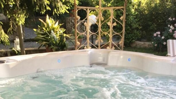 A hot tub with two glasses of white wine and a plate of strawberries and roses.