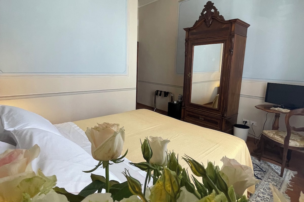 A hotel room with a large bed, a wooden wardrobe, a chandelier, and a mirror.