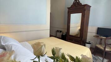 A hotel room with a large bed, a wooden wardrobe, a chandelier, and a mirror.