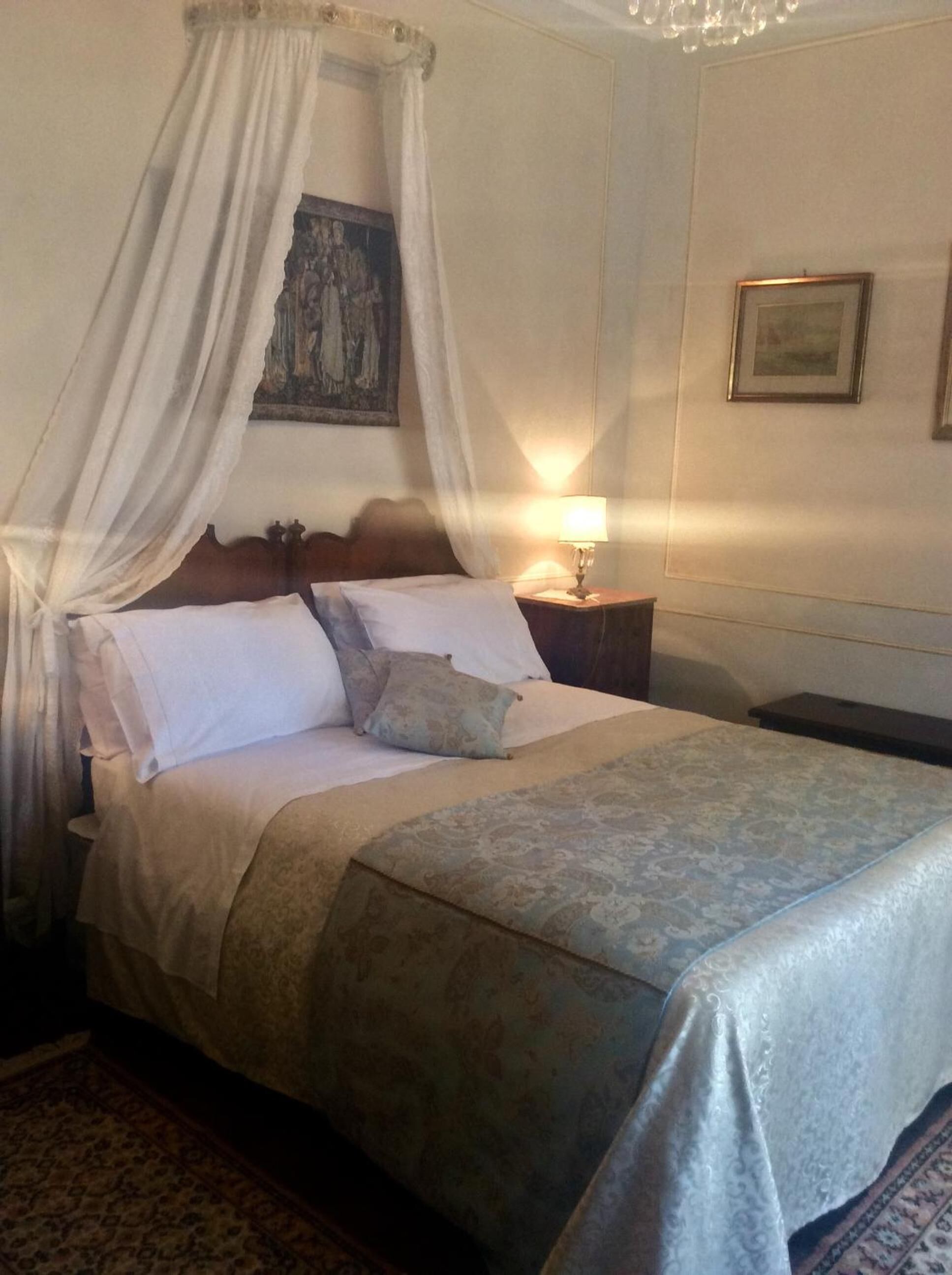 A neatly made bed with a canopy, a bedside lamp, and a framed picture on the wall.
