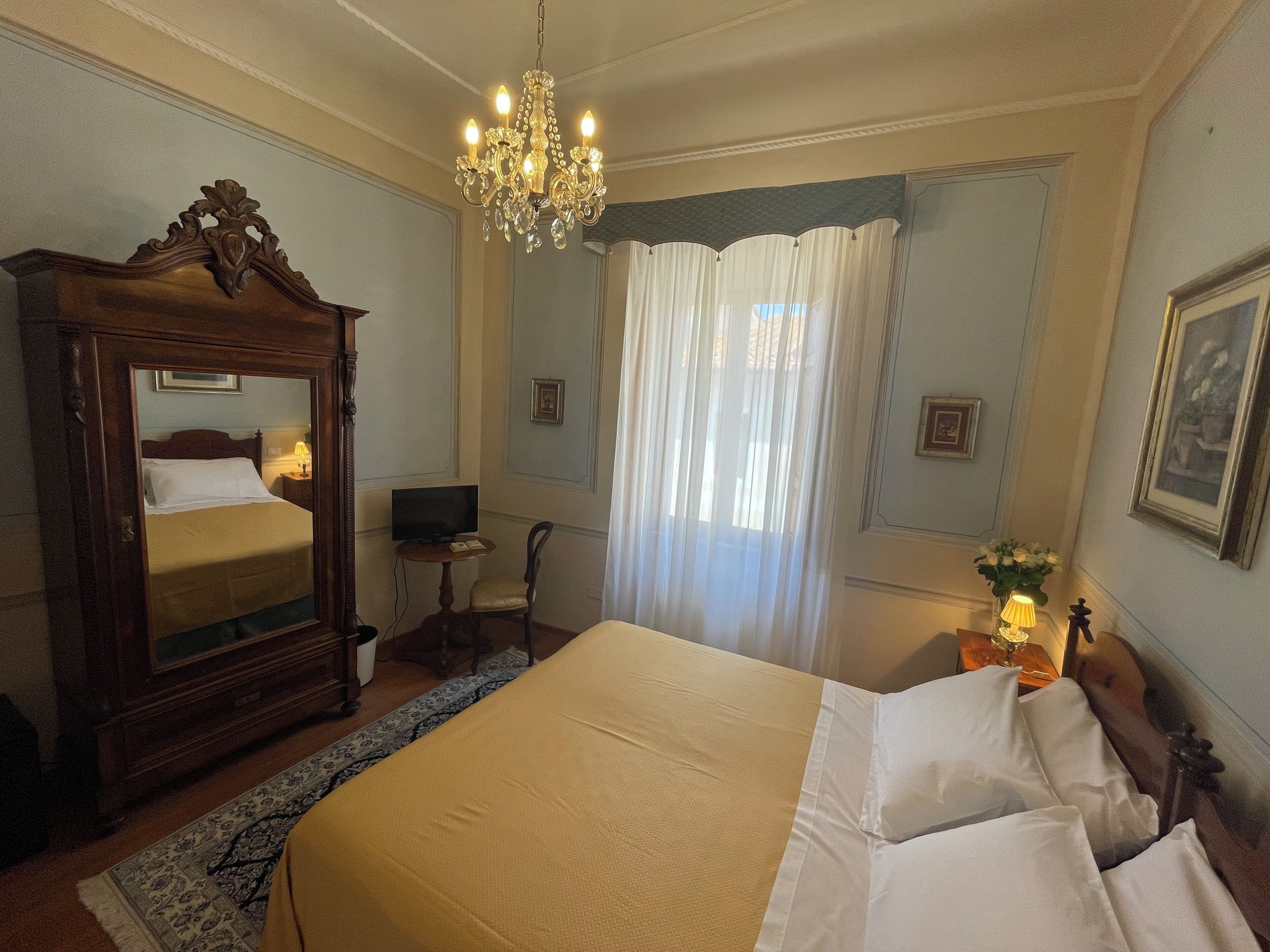 Ein Hotelzimmer mit einem großen Bett, einem Holzschrank, einem Schreibtisch mit Stuhl, einem Fernseher und einer Kandelaber.