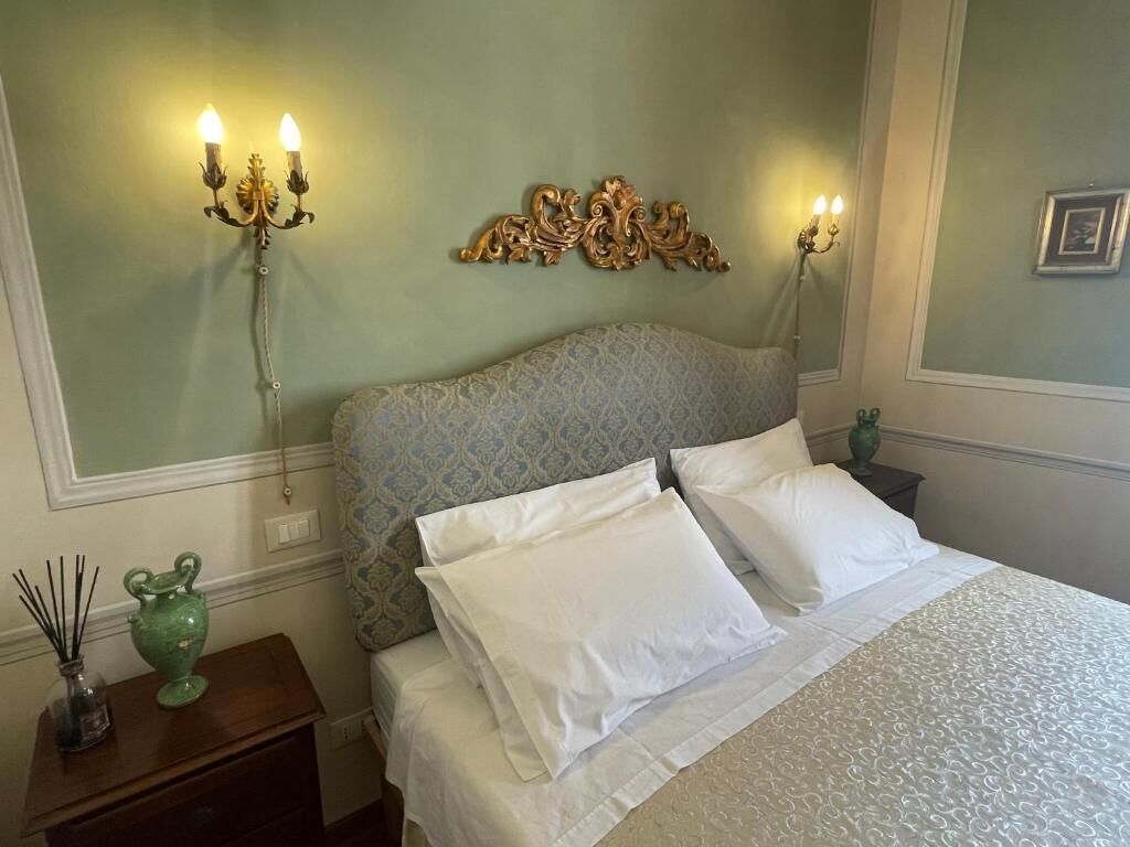 A bedroom with a patterned headboard, two bedside lamps, a green vase, and a bed with white bedding.