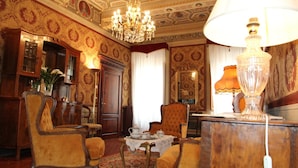 A richly decorated room with ornate wallpaper, a chandelier, and classic furniture.