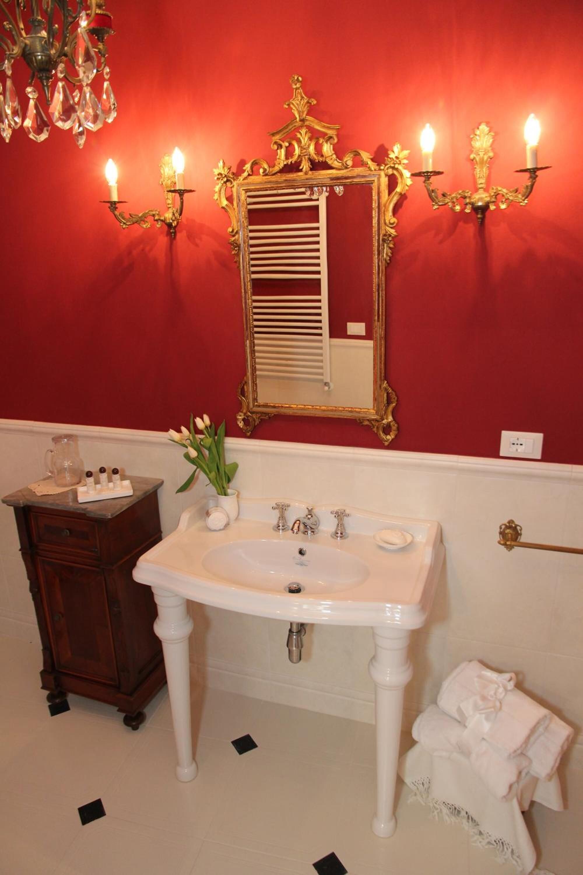 Un bagno con un lavandino bianco, uno specchio con cornice dorata e un lampadario.