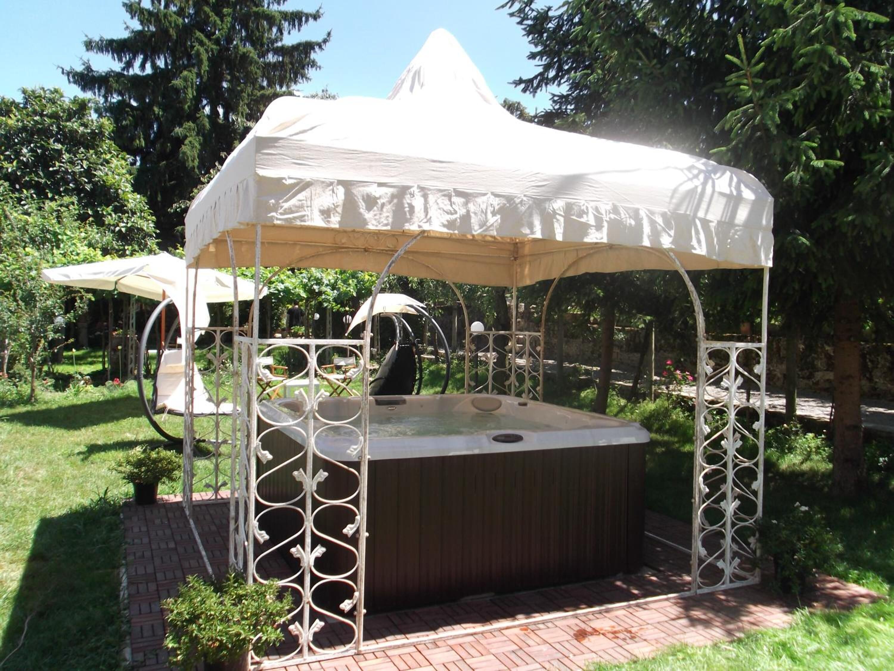 A hot tub with a white canopy and metal railings, surrounded by greenery and a brick pathway.