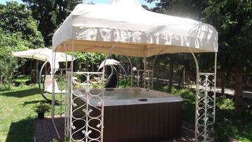 A hot tub with a white canopy and metal railings, surrounded by greenery and a brick pathway.