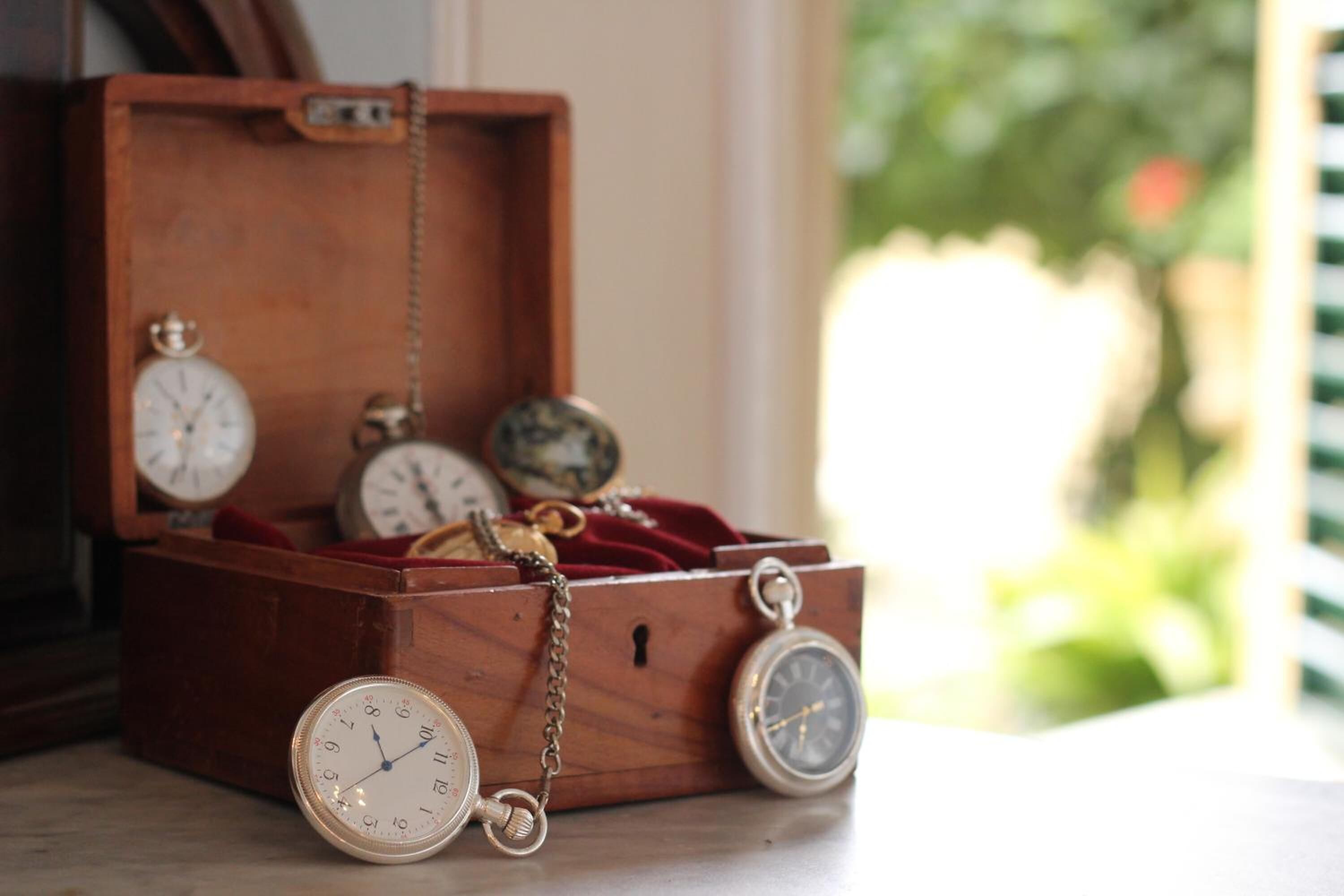 Een houten doos met een ketting en drie zakhorloges erin.
