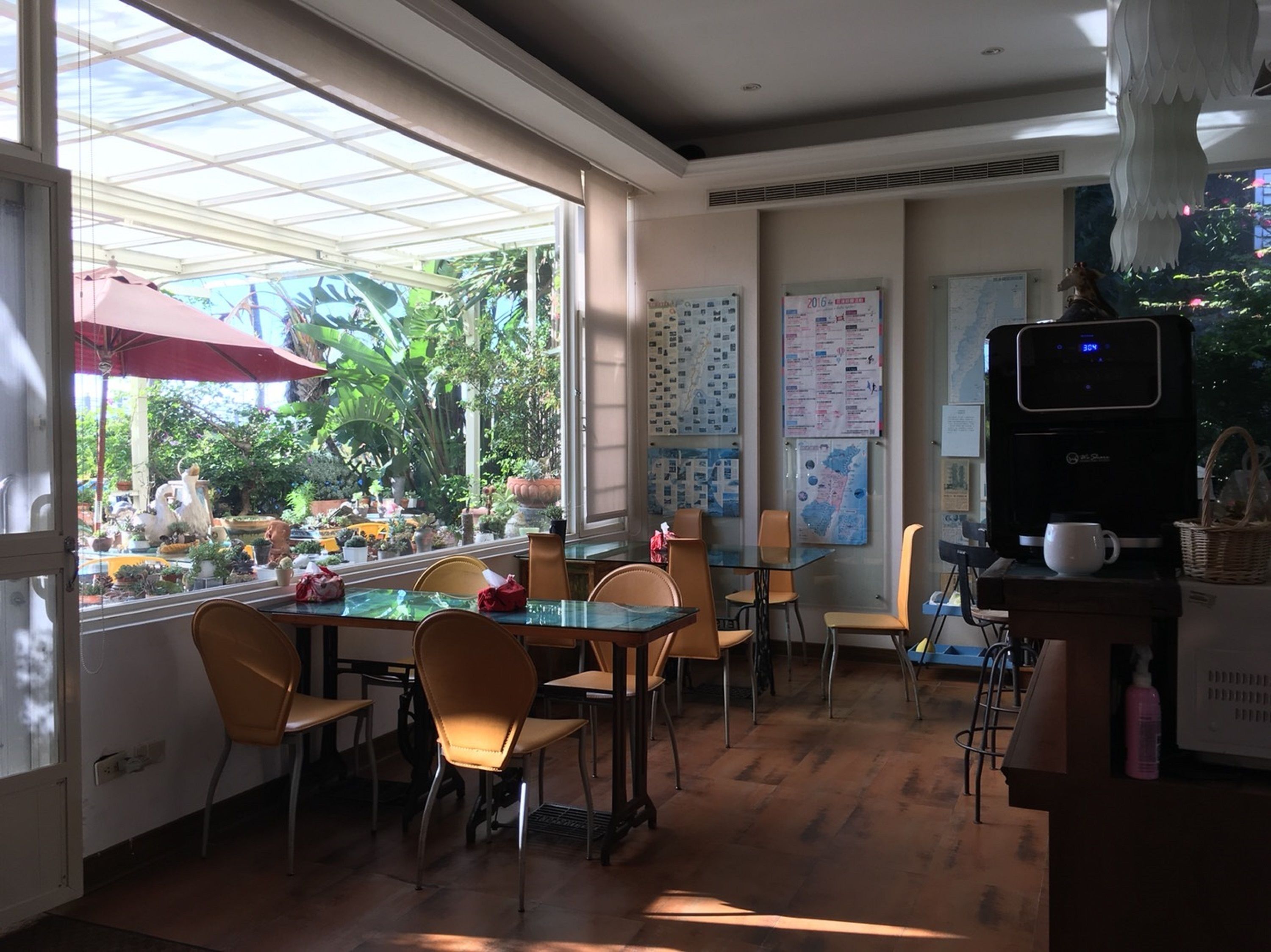 A café with a glass table, chairs, a coffee machine, and a view of a garden through large windows.