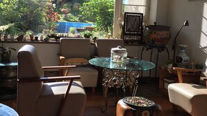 Una habitación iluminada por el sol con una mesa de vidrio, dos sillas, un taburete pequeño y una planta en maceta.