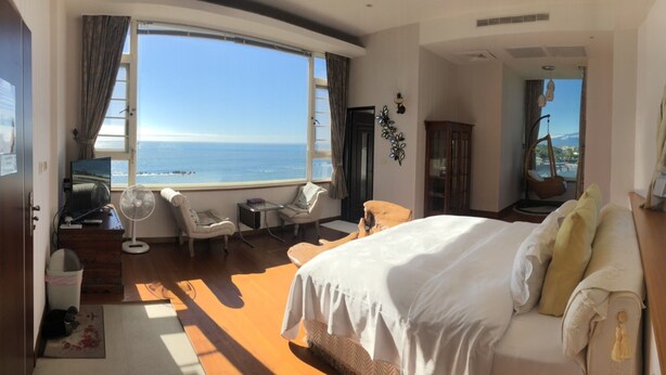 Habitación de hotel con una cama grande, un área de estar con vista al mar y suelo de madera.