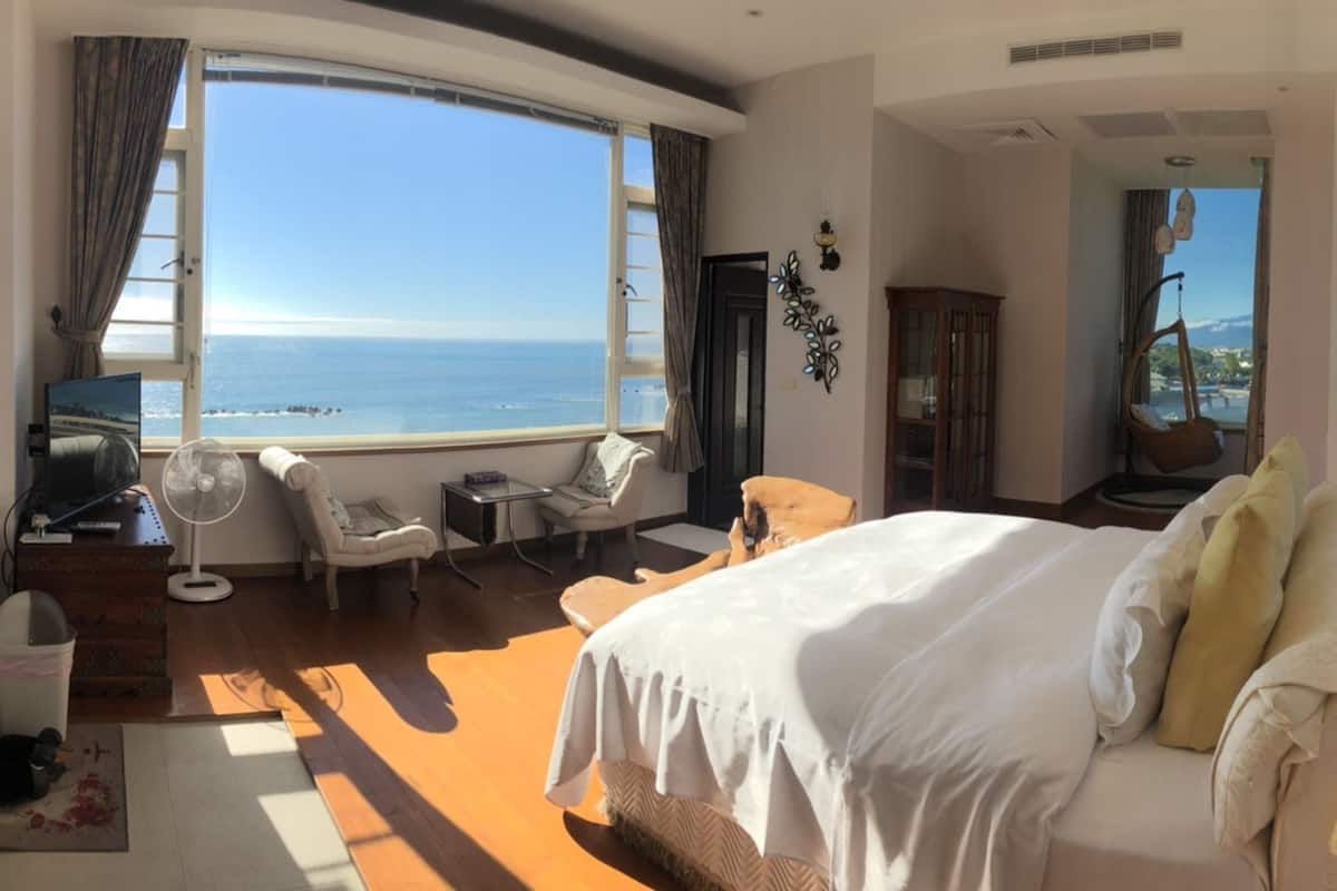 A hotel room with a large bed, a sitting area with a view of the sea, and a wooden floor.