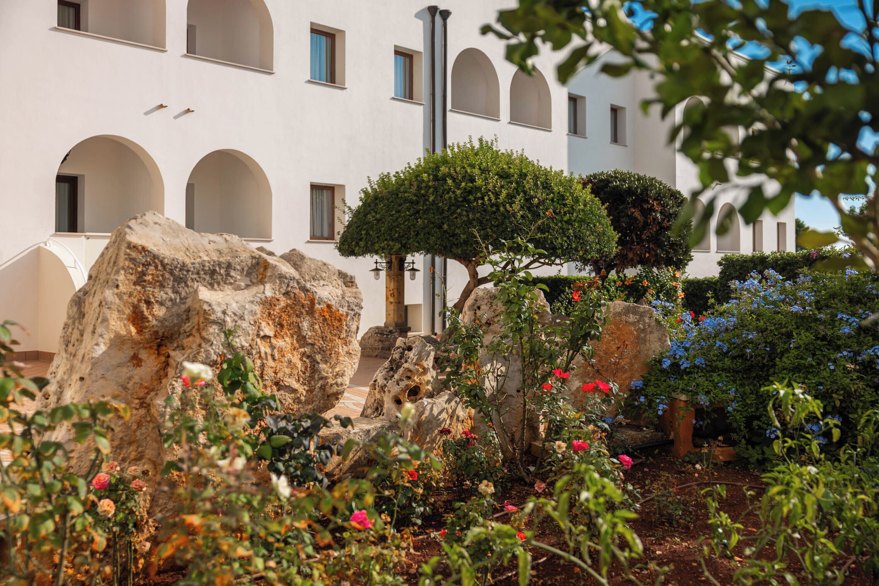 A courtyard with a white building featuring arched windows and a stone wall.