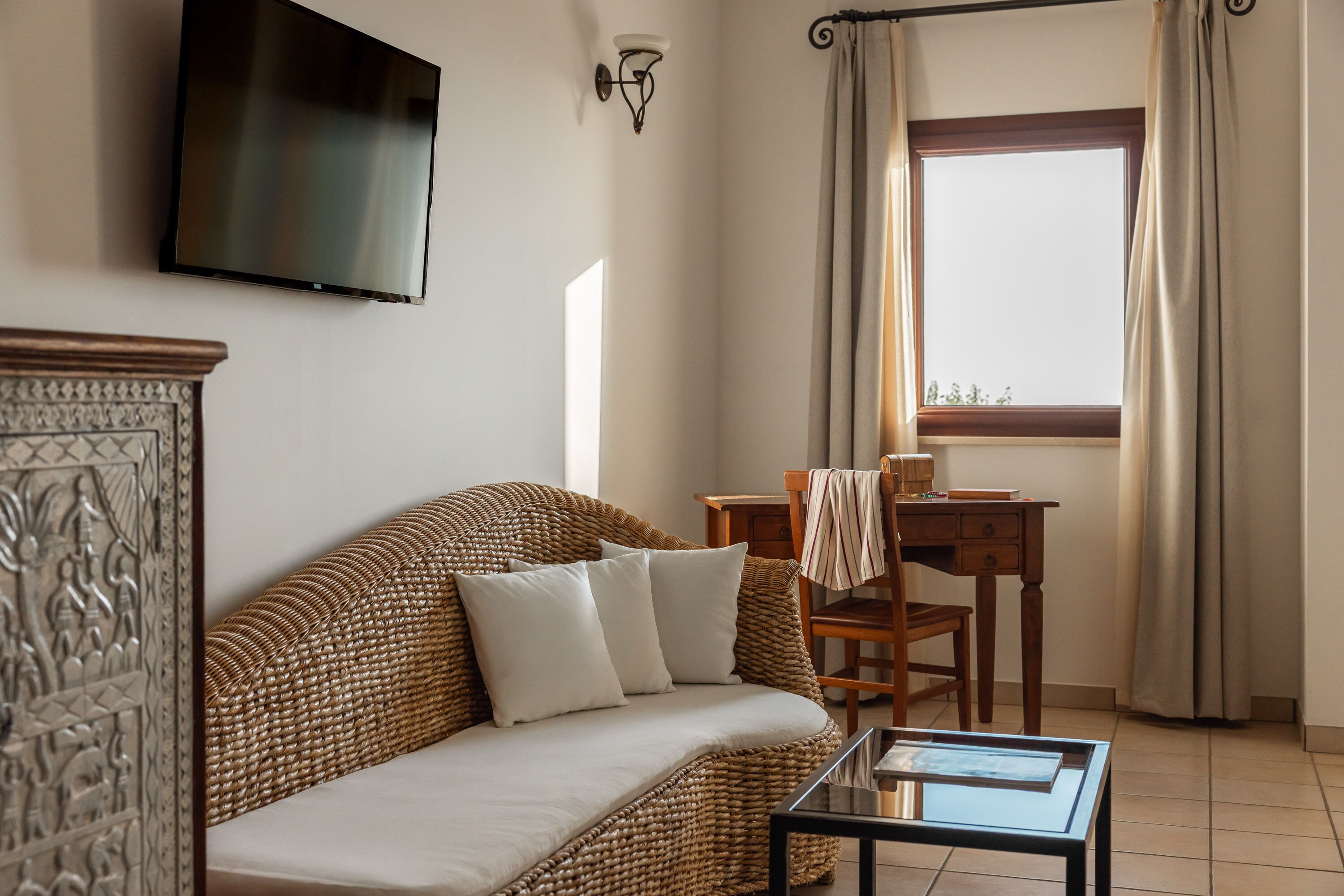 A living room with a wicker sofa, a flat-screen TV, a wooden table, and a window with curtains.